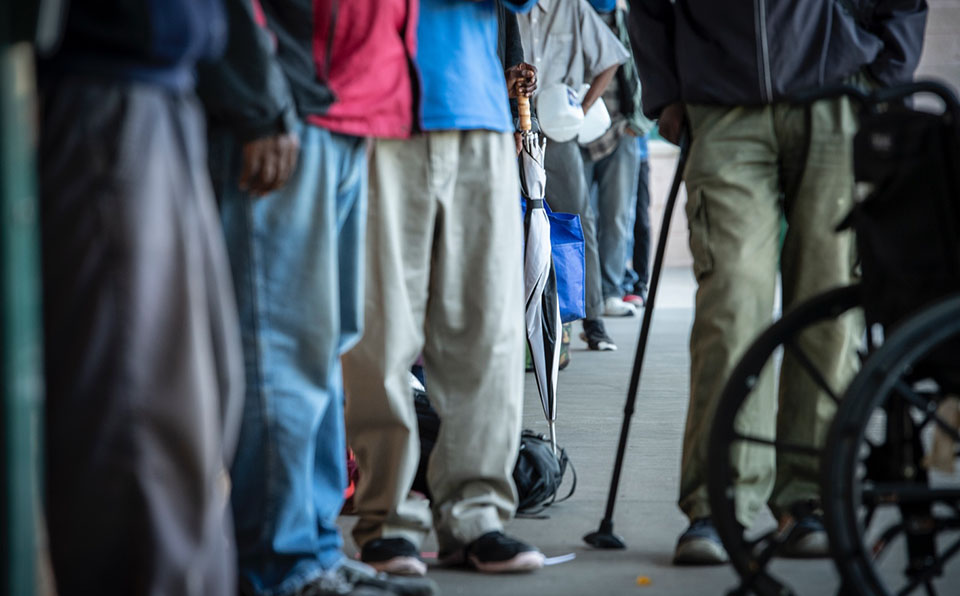 Panoramic image of people lined up, their legs visible as they walk towards a door.