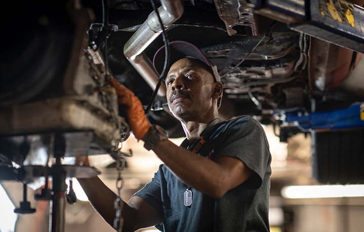 Angled view of a mechanic inspecting the undercarriage of a suspended vehicle.